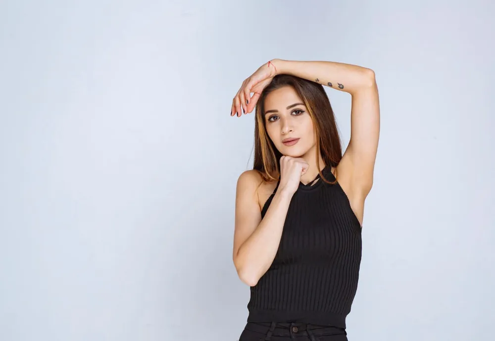Jeune femme brune en débardeur noir, bras levé, aisselle et avant-bras dégagés