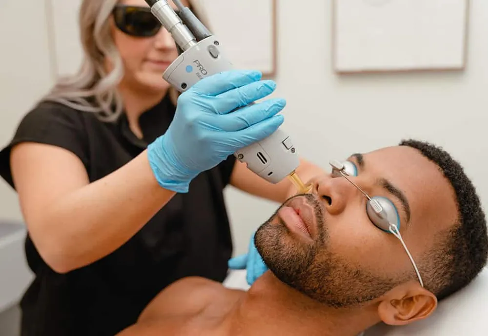 Praticienne en gants bleus passant le laser sur la joue d'un homme qui porte des lunettes de protection