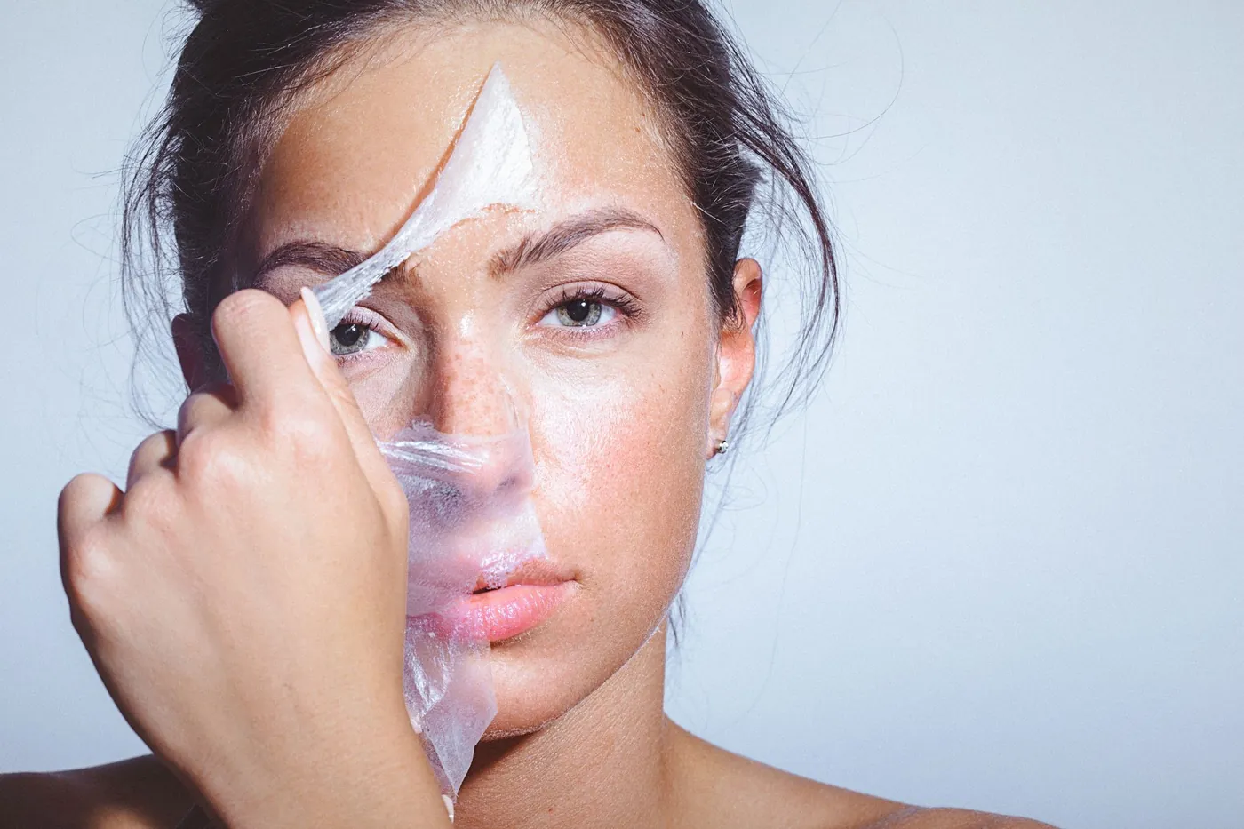 Femme qui retire un film transparent de peeling de sa joue, peau lisse et nette