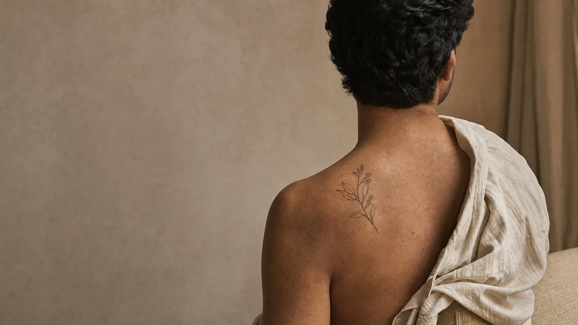 Homme de dos, épaule nue, petit tatouage floral fin entre l'omoplate et la nuque avant un détatouage laser